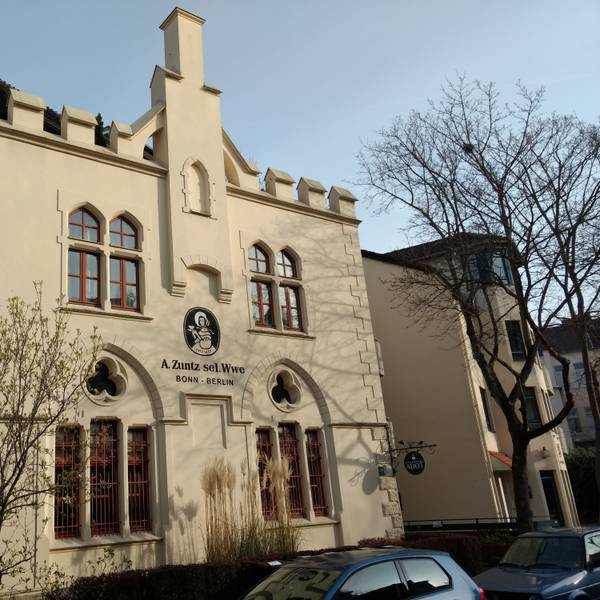 Das Gebäude der ehemaligen Kaffeerösterei in der Bonner Südstadt. Es ist das bekannte Logo zu sehen: Eine Frau mit Kleid und Schutenhut hält eine Kaffeetasse mit Untertasse in der Hand. Darunter die Aufschrift: „A. Zuntz sel. Wwe / Bonn – Berlin“.