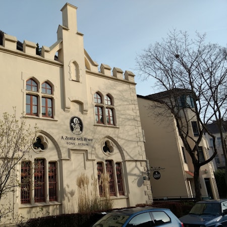 Das Gebäude der ehemaligen Kaffeerösterei in der Bonner Südstadt. Es ist das bekannte Logo zu sehen: Eine Frau mit Kleid und Schutenhut hält eine Kaffeetasse mit Untertasse in der Hand. Darunter die Aufschrift: „A. Zuntz sel. Wwe / Bonn – Berlin“.