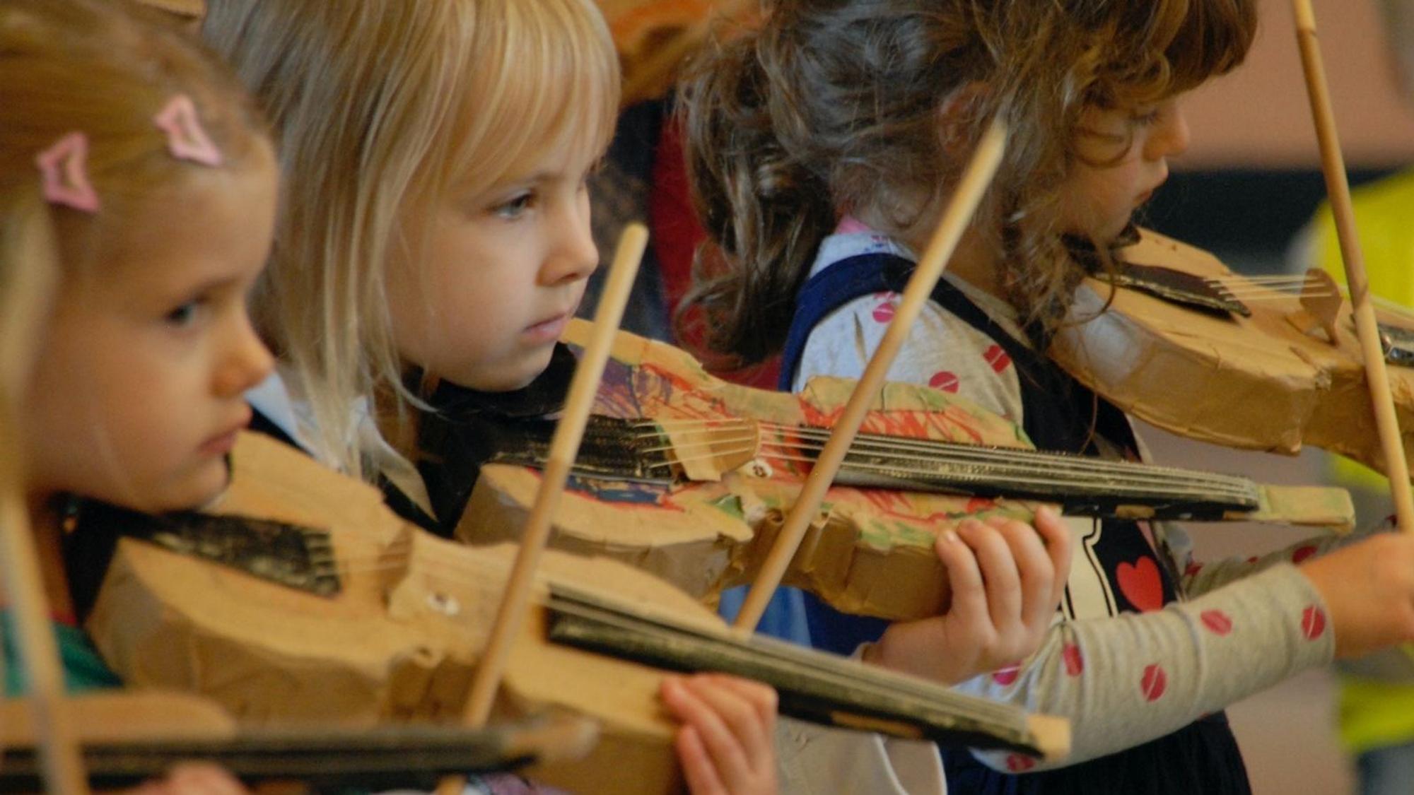 Drei Mädchen spielen Geige mit einem Pappinstrument.