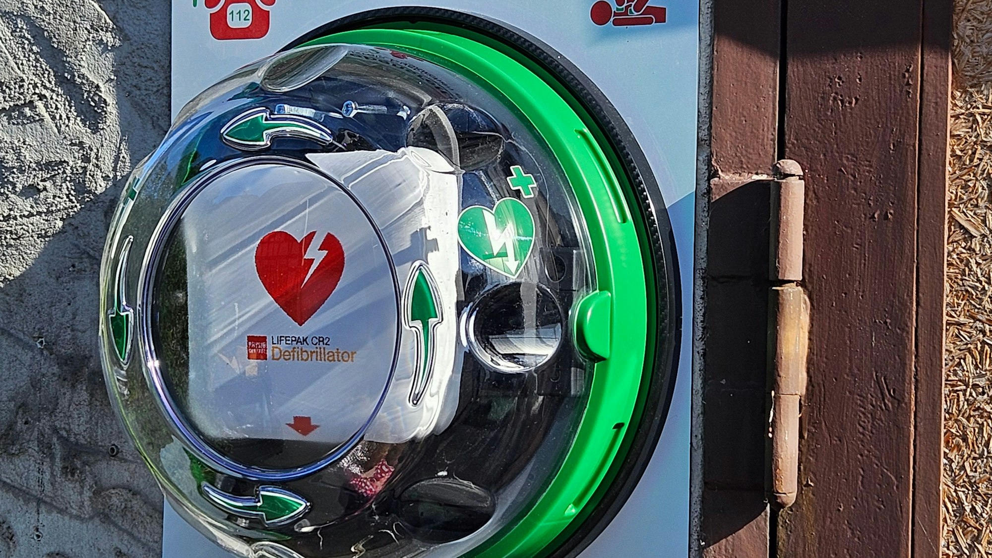 Das Bild zeigt einen Defibrillator, der an einer Wand angebracht ist.