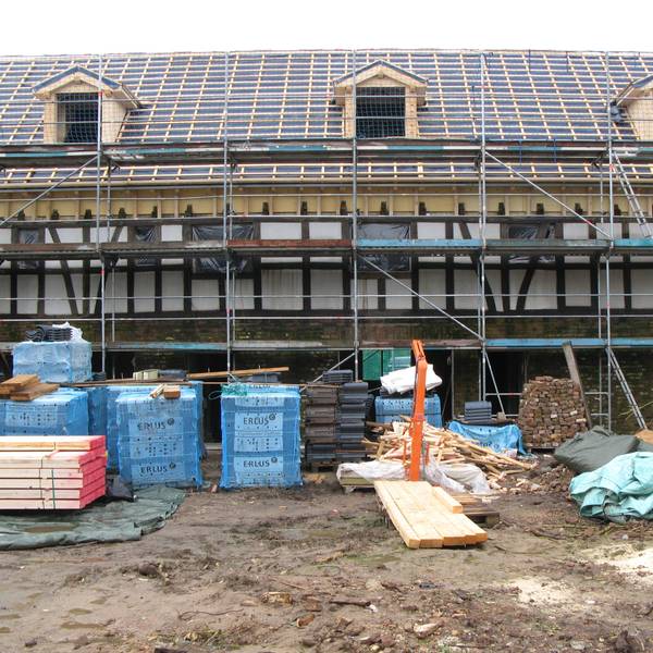 Ein langgestrecktes Fachwerkgebäude ist eingerüstet, das Dach ist für die Neueindeckung vorbereitet.