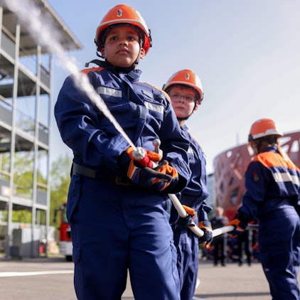 Kinder in Feuerwehruniformen richten den Schlauch auf das Ziel.