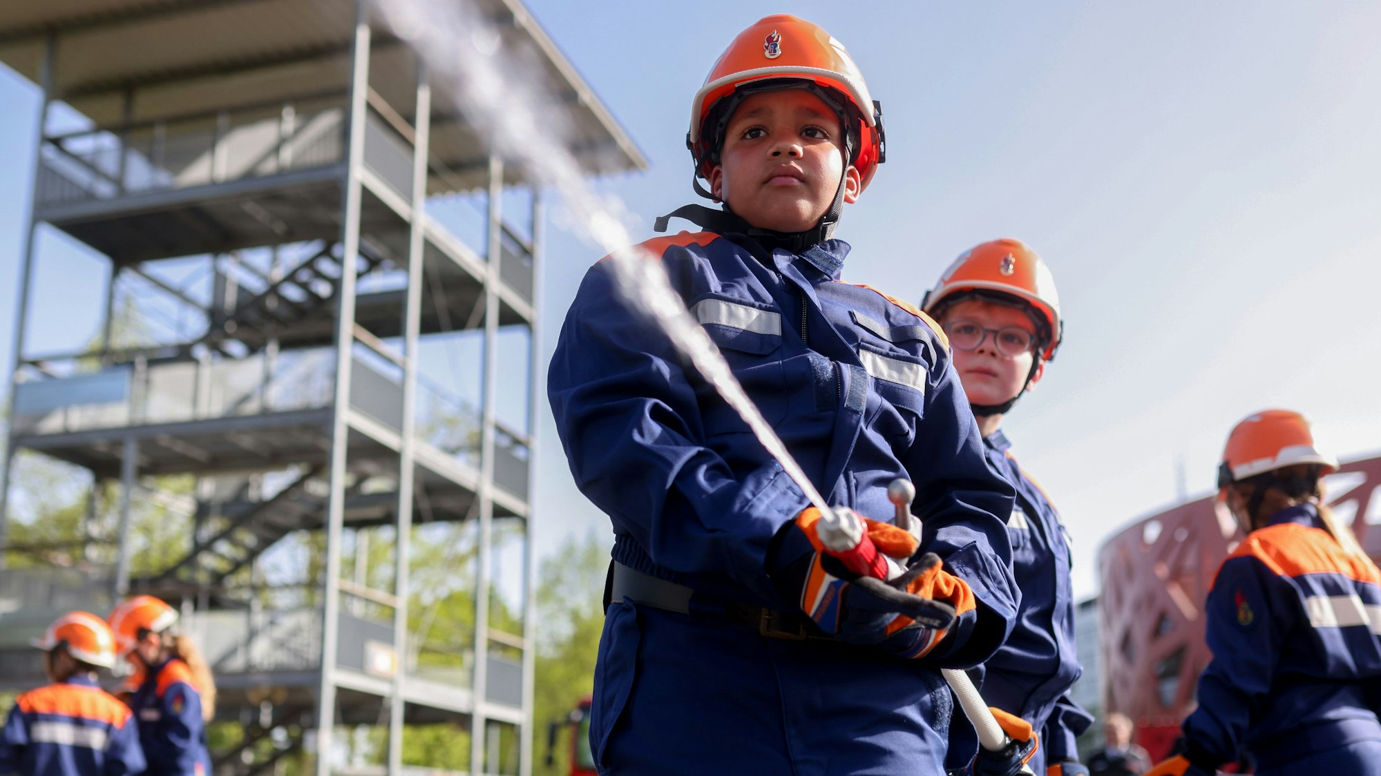 Kinder in Feuerwehruniformen richten den Schlauch auf das Ziel.