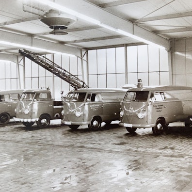 Schwarzweißbild von VW-Bullis mit Blaulicht, die 1962 in einer Halle in einer Reihe stehen.
