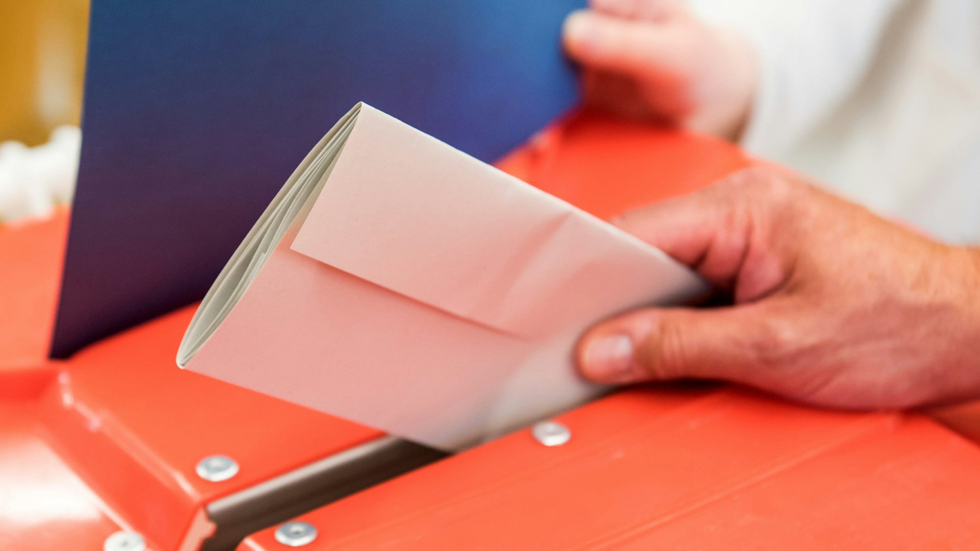 Ein Wahlhelfer steckt in einem Wahllokal den Stimmzettel eines Wählers in eine Wahlurne.