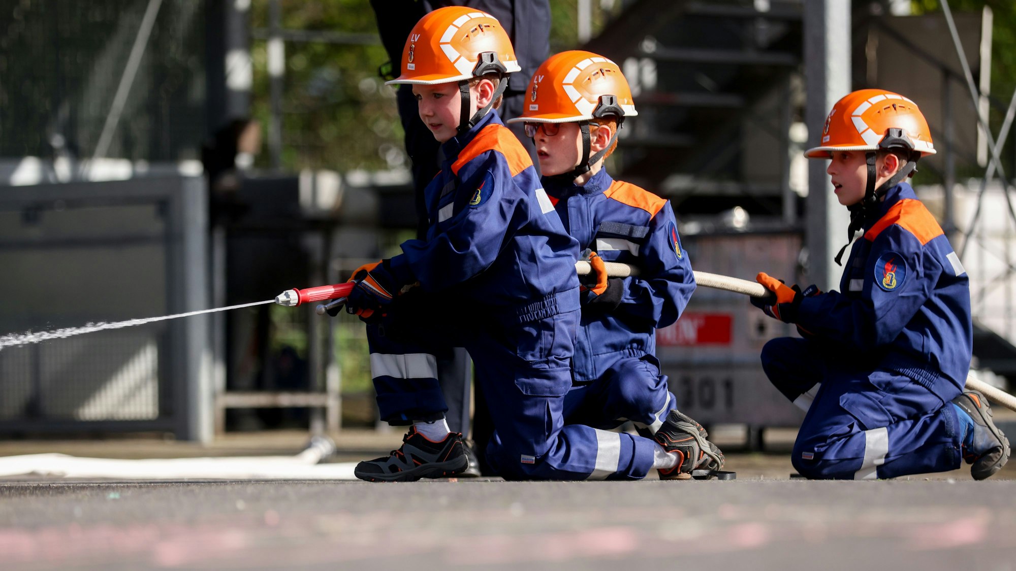Drei Mitglieder der Kinderfeuerwehr mit Spritze und Schlauch.