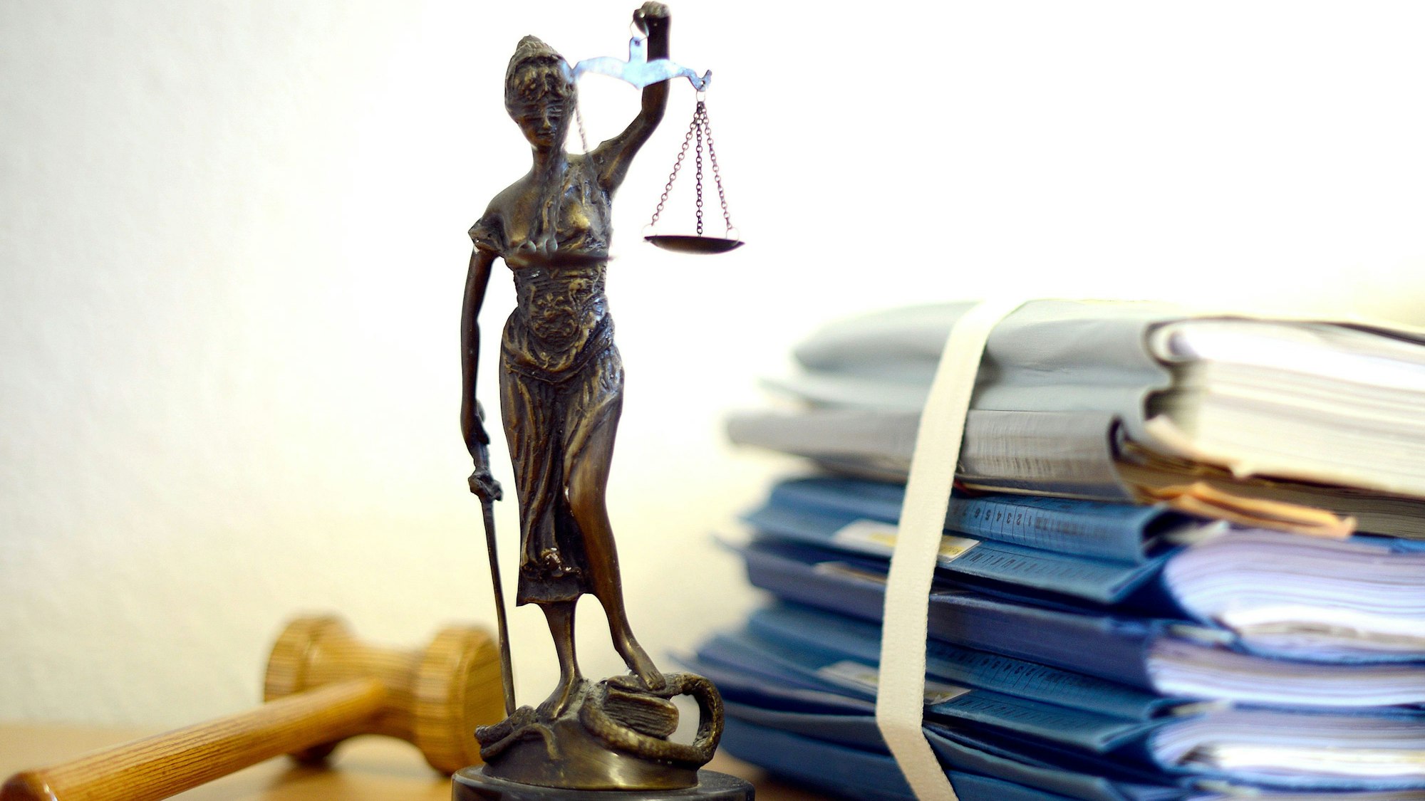 Die modellhafte Nachbildung der Justitia steht in einem Raum eines Richters neben einem Holzhammer und einem Aktenstapel.