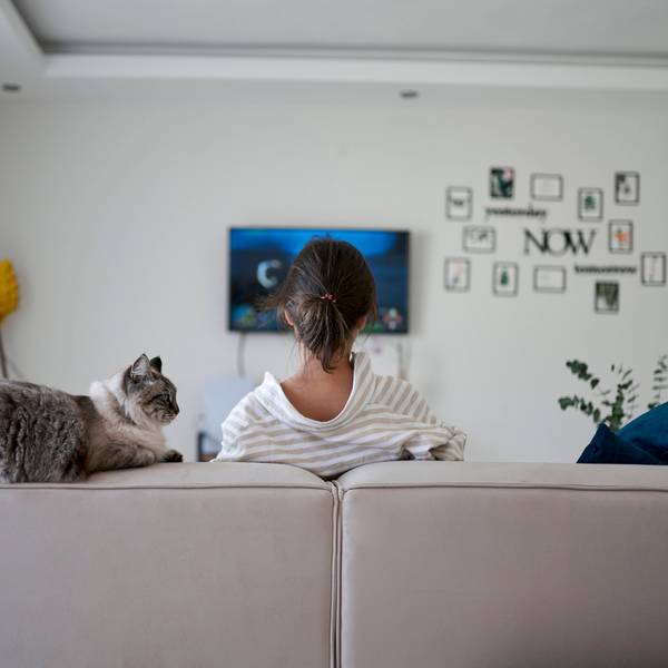 Foto einer Frau die auf dem Sofa vor eine Fernseher sitzt, zusammen mit einer Katze.