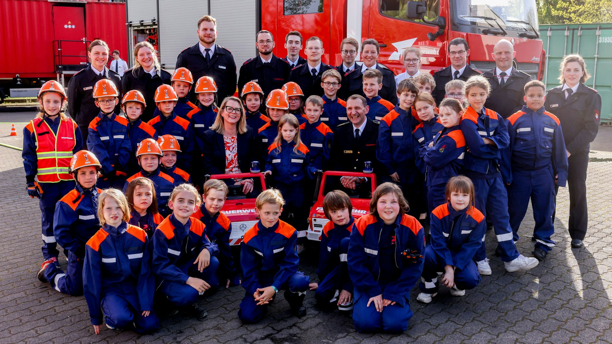 Mitglieder der Kinderfeuerwehr posieren mit Stadtdirektorin Andrea Blome und dem Leiter der Feuerwehr, Dr. Christian Miller, vor einem Wagen der Feuerwehr.