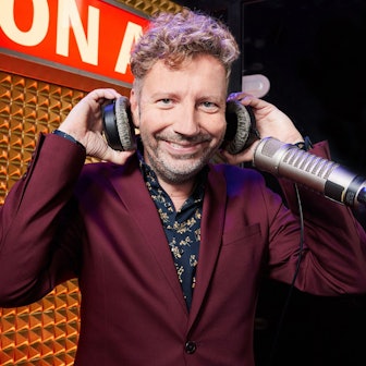 Thorsten Schorn steht an einem Mikrofon, er hat Kopfhörer in der Hand und trägt einen bordeauxfarbenen Anzug.