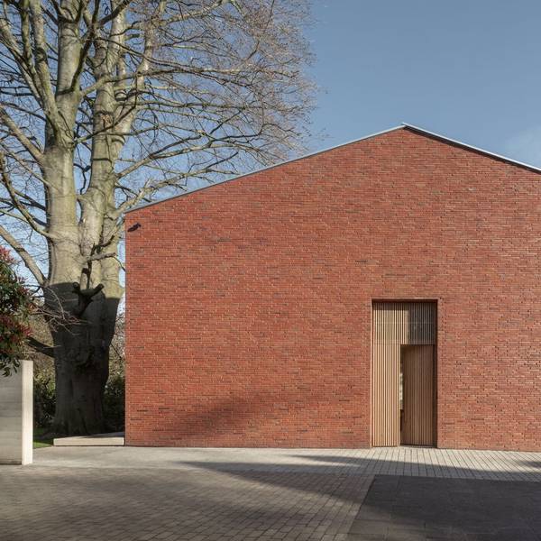 Ein Ziegelhaus ohne Fenster zur Straße steht neben einem alten Baum.