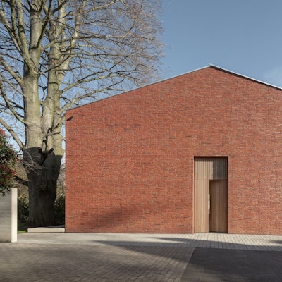 Ein Ziegelhaus ohne Fenster zur Straße steht neben einem alten Baum.