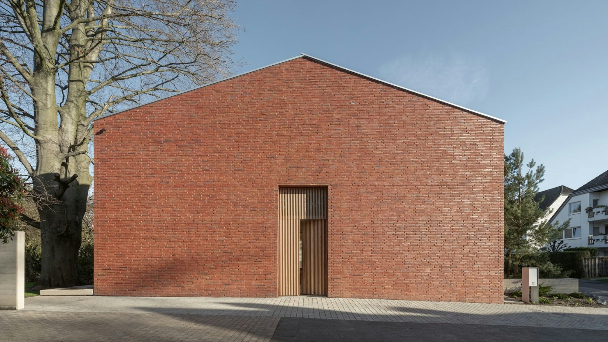 Ein Ziegelhaus ohne Fenster zur Straße steht neben einem alten Baum.