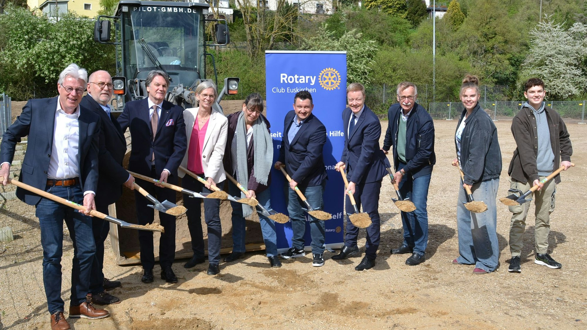 Vertreter des Rotary-Clubs und der Schule halten Schaufeln in den Händen, die mit Erde gefüllt sind.