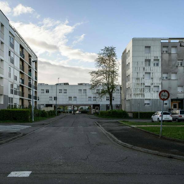 Plattenbauten und eine leere Straße befinden sich vor einem leicht bewölkten Himmel.