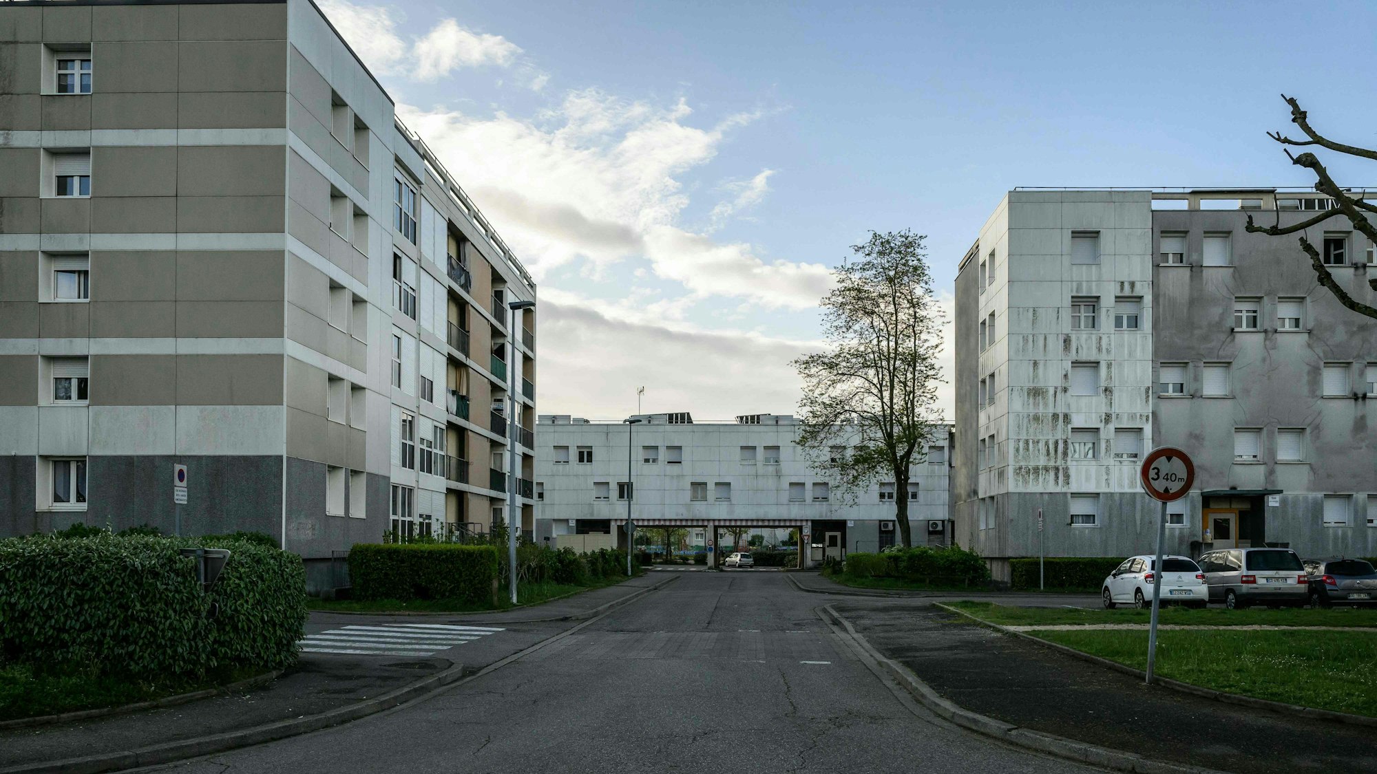 Plattenbauten und eine leere Straße befinden sich vor einem leicht bewölkten Himmel.