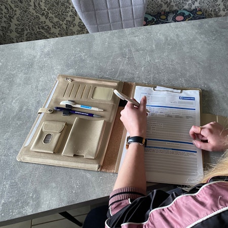 Auf einem Tisch liegt eine beigefarbene Mappe. Darin befinden sich Formulare des Weißen Rings. Yasmin Fuhl füllt die Formulare mit einem Kugelschreiber aus.