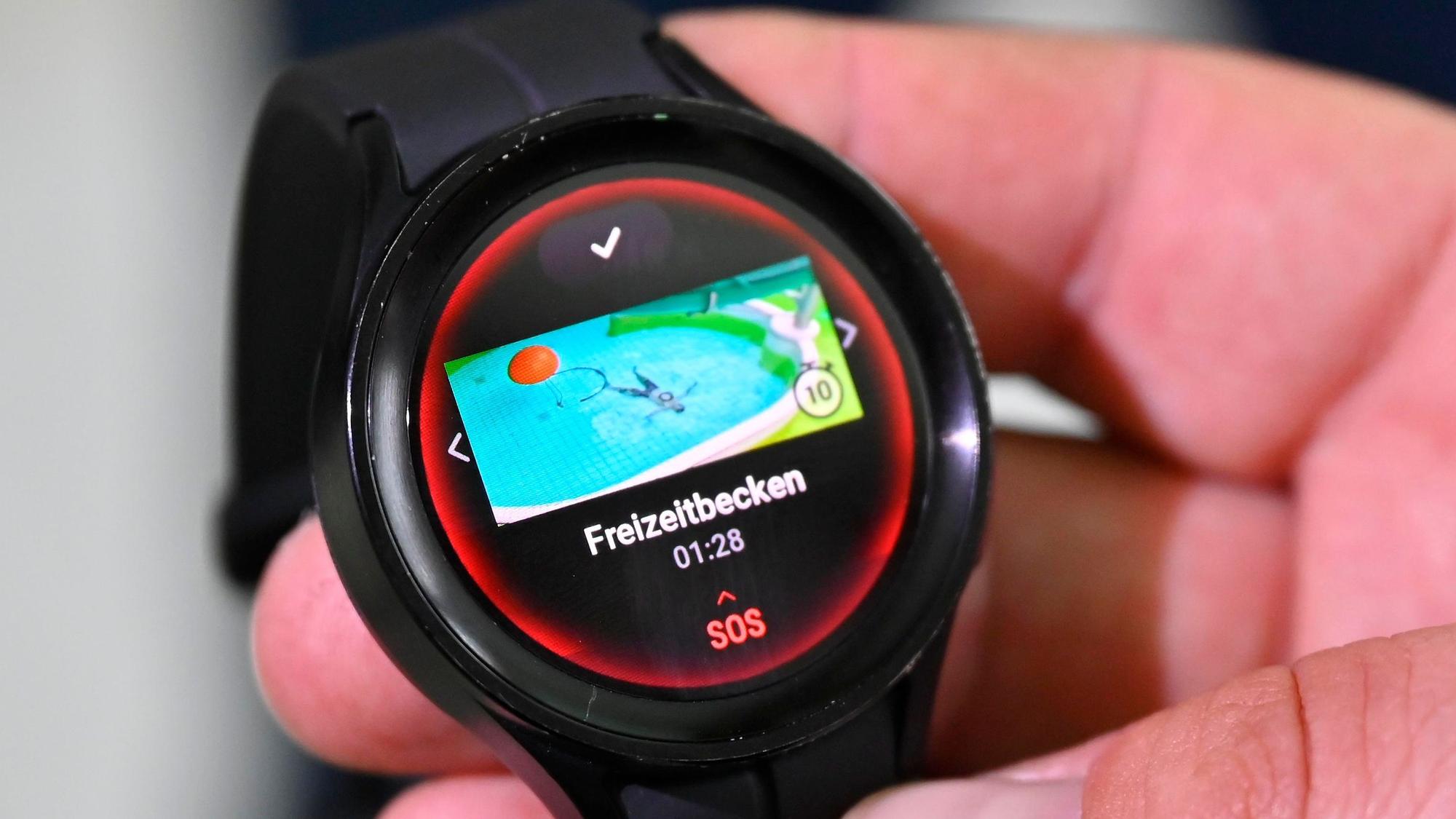 Eine Hand hält eine digitale Uhr, auf der ein Schwimmbecken und das Wort SOS zu sehen sind.