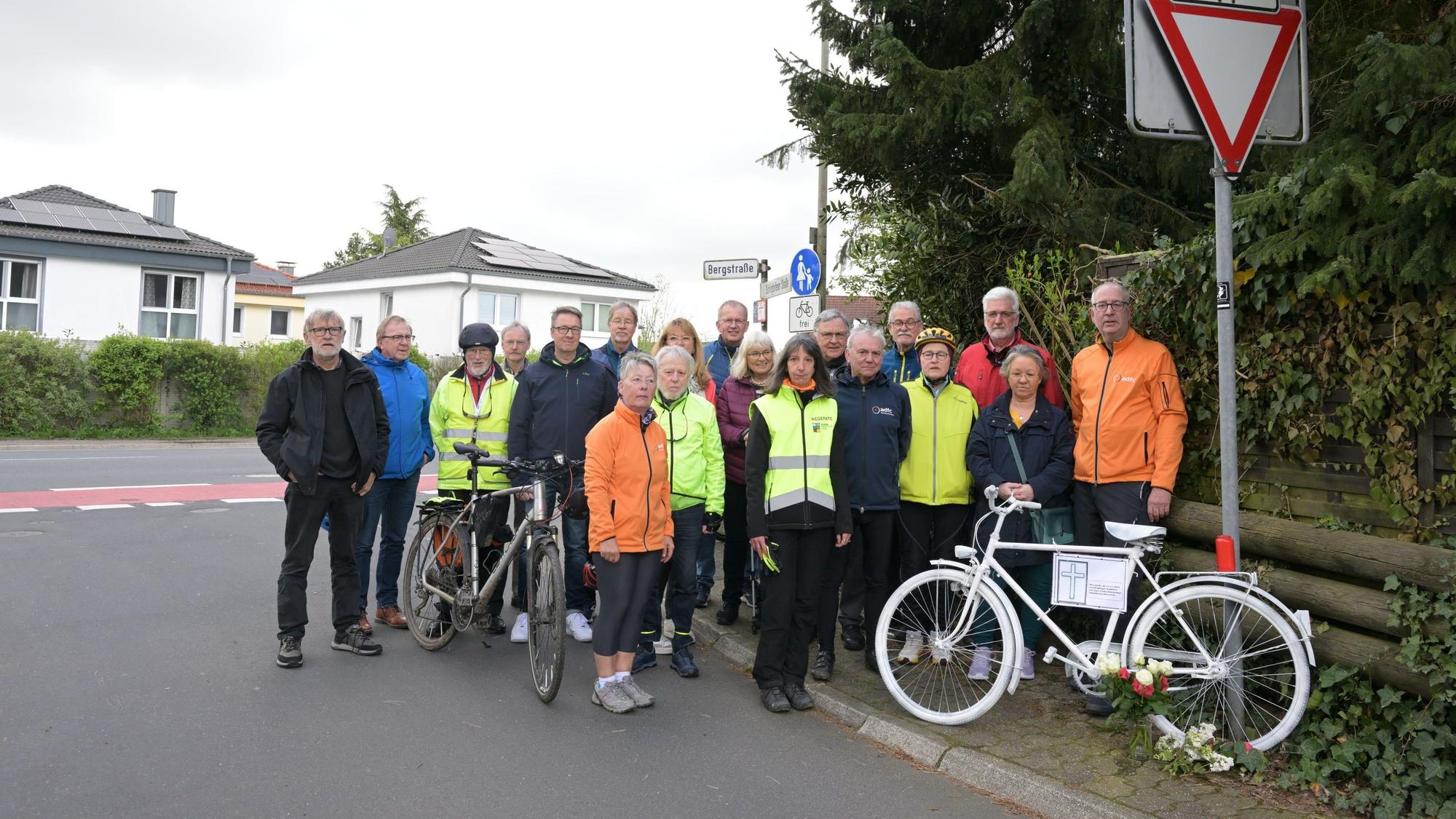 Radfahrer stehen an einem weiß lackierten Mahnrad. Davor Blumen und eine Kerze.