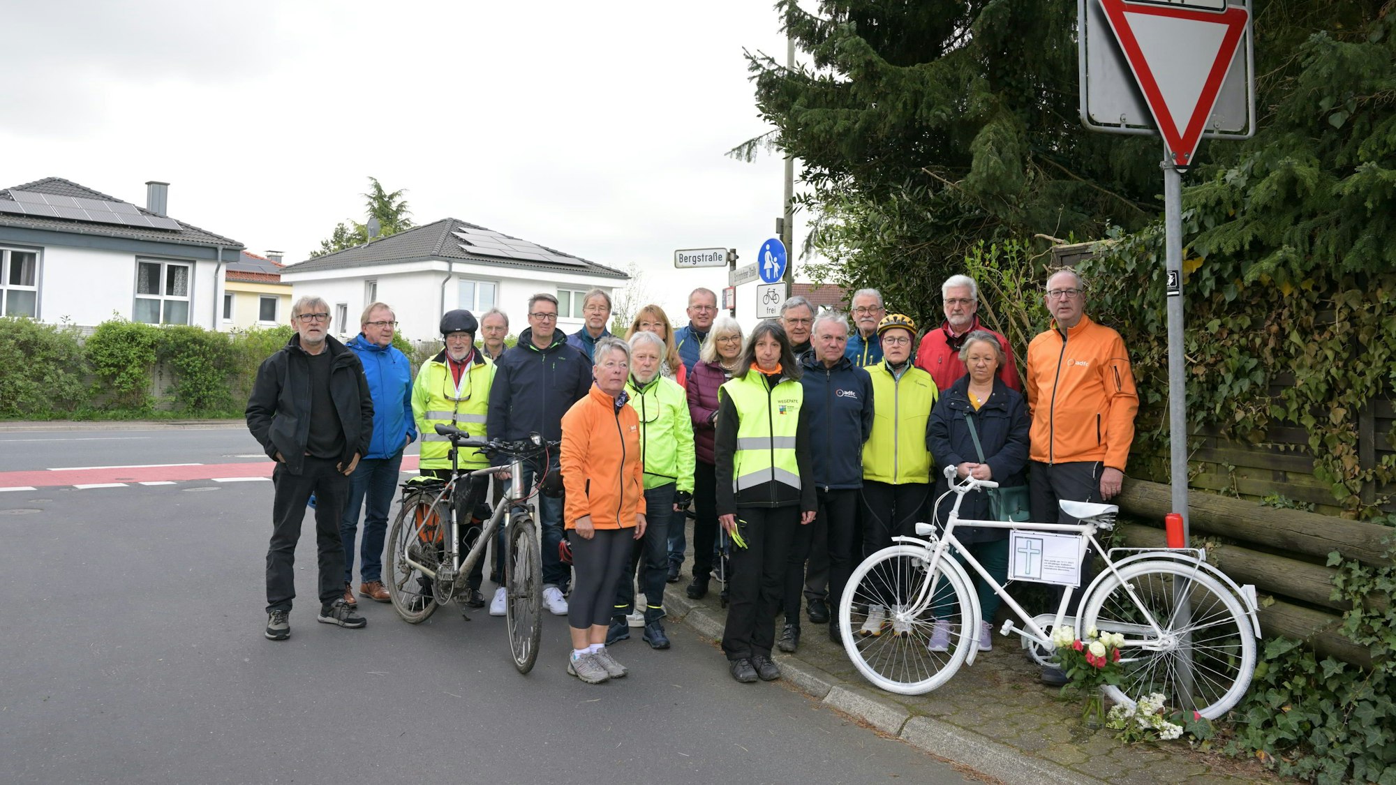 Radfahrer stehen an einem weiß lackierten Mahnrad. Davor Blumen und eine Kerze.