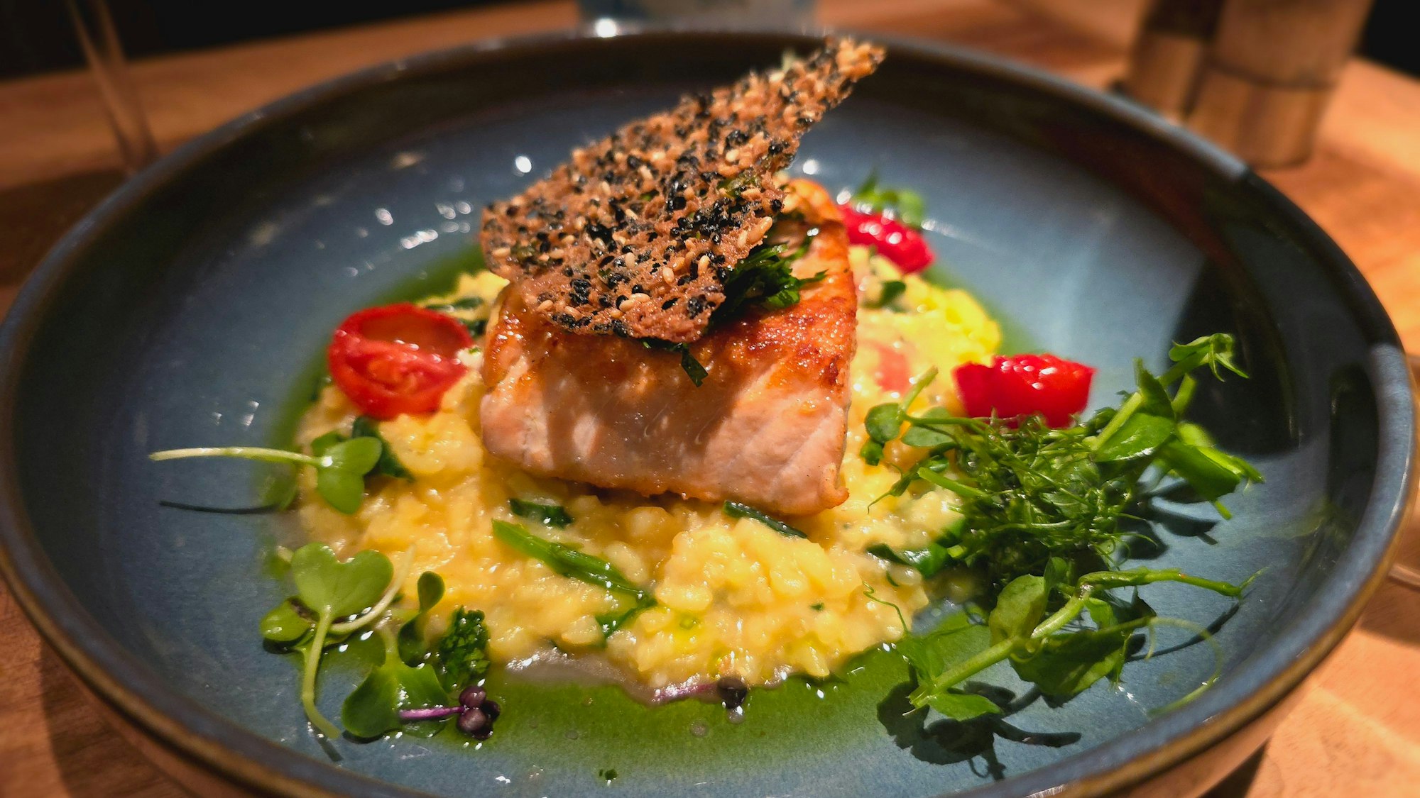 Risotto mit Lachsfilet, jungem Blattspinat, Safran und Kirschtomaten auf einem Teller angerichtet