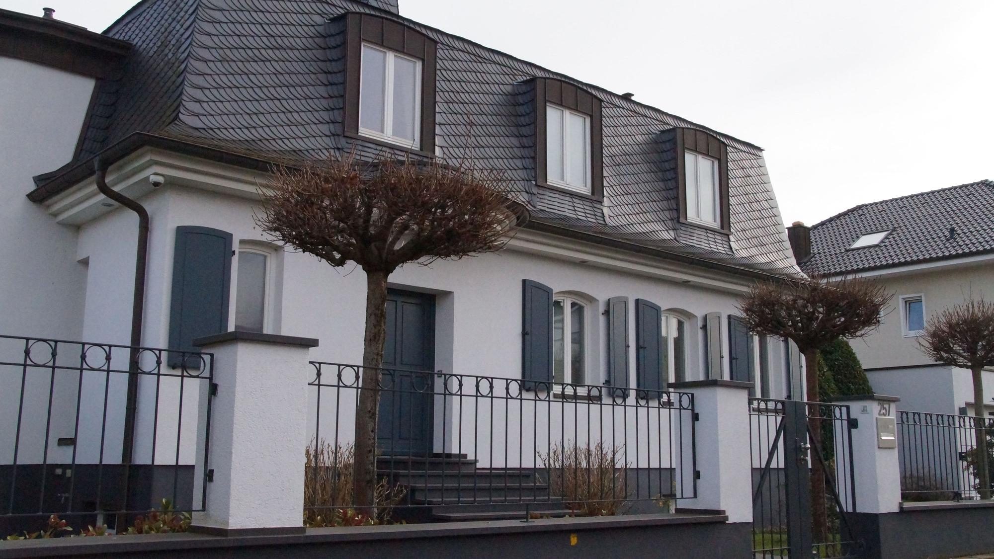 Eine weiße Villa, mit dunklen Fensterläden und dunkel gedecktem Dach.
