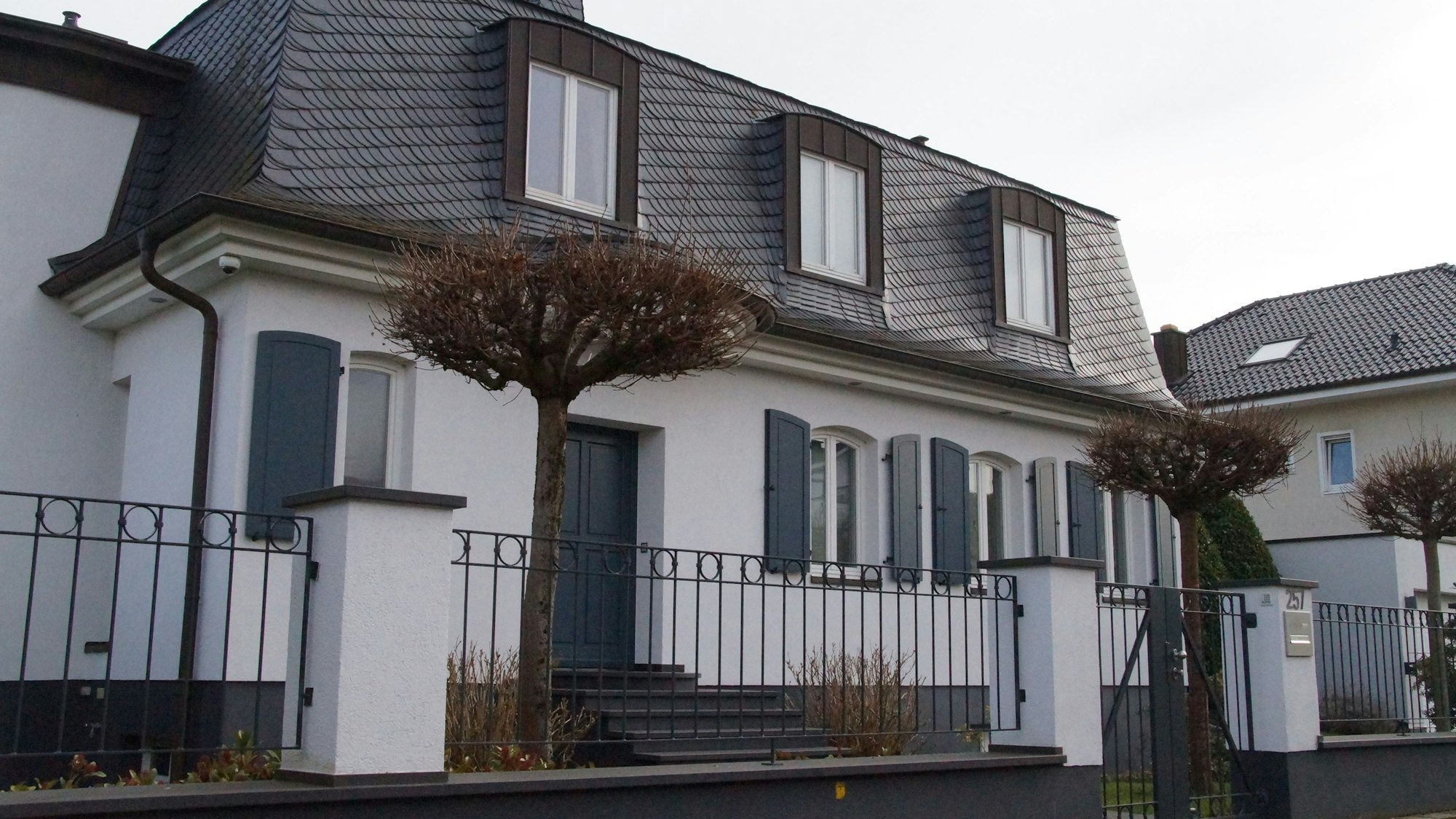 Eine weiße Villa, mit dunklen Fensterläden und dunkel gedecktem Dach.