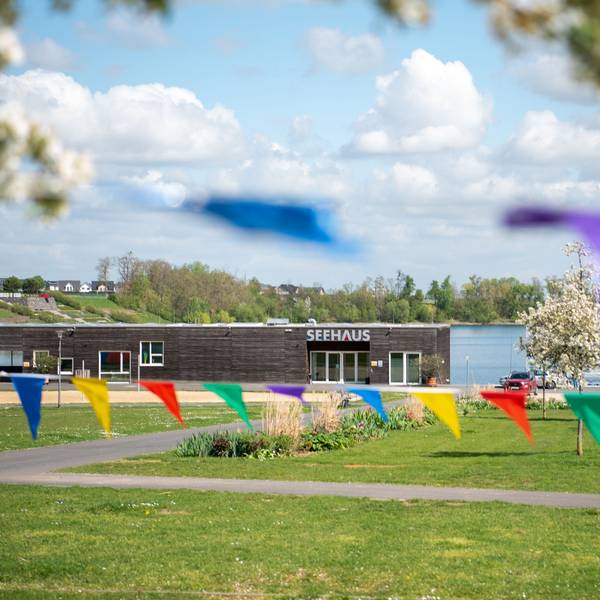 Bunte Wimpel hängen zwischen blühenden Obstbäumen auf einer Wiese vor dem Seehaus im Seepark Zülpich.