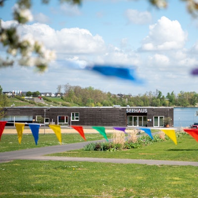 Bunte Wimpel hängen zwischen blühenden Obstbäumen auf einer Wiese vor dem Seehaus im Seepark Zülpich.