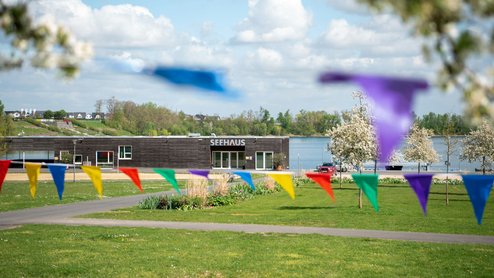Bunte Wimpel hängen zwischen blühenden Obstbäumen auf einer Wiese vor dem Seehaus im Seepark Zülpich.