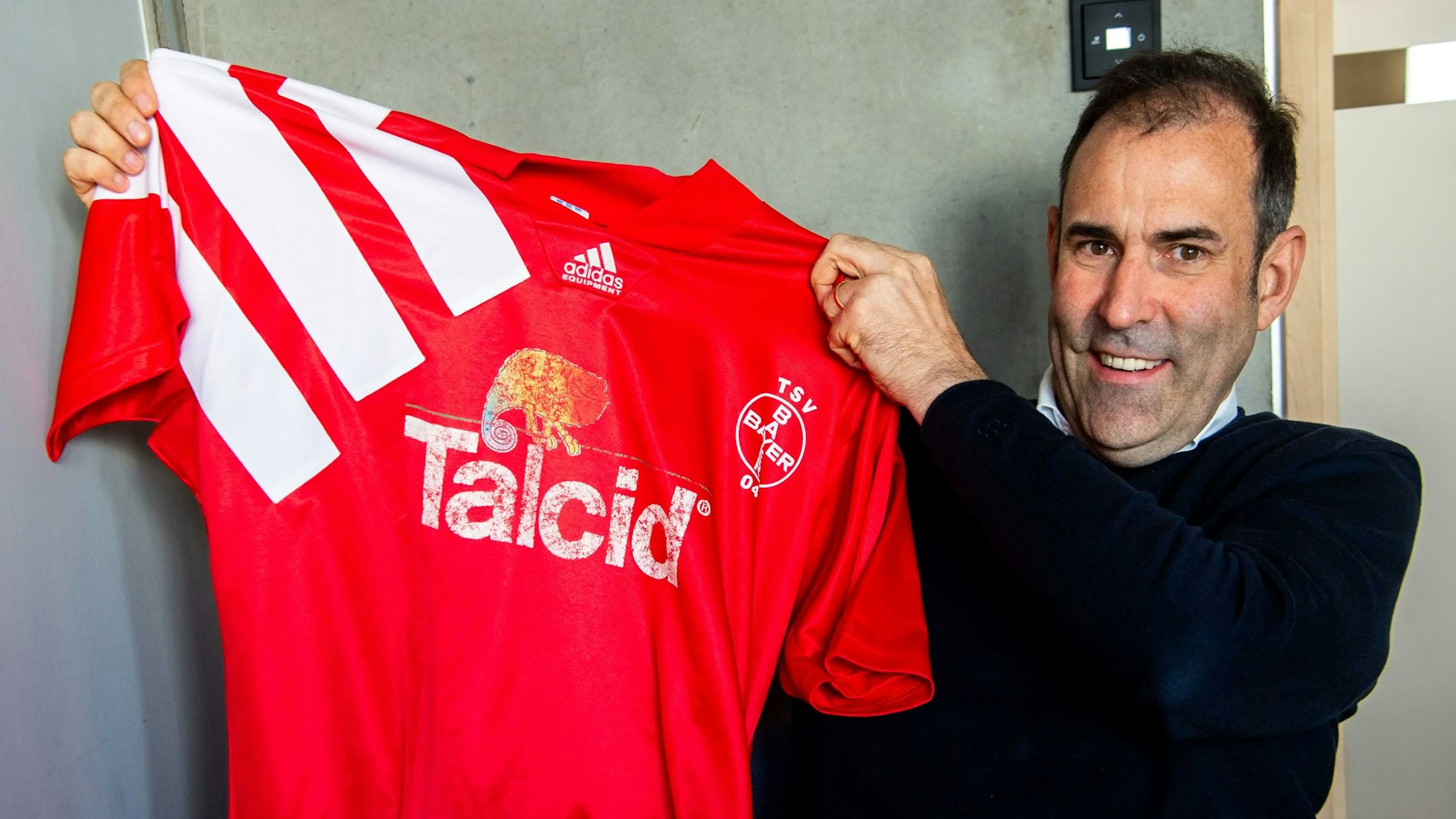 Das Bild zeigt Johannes Winckler, wie er ein älteres Trikot von Bayer Leverkusen hochhält.