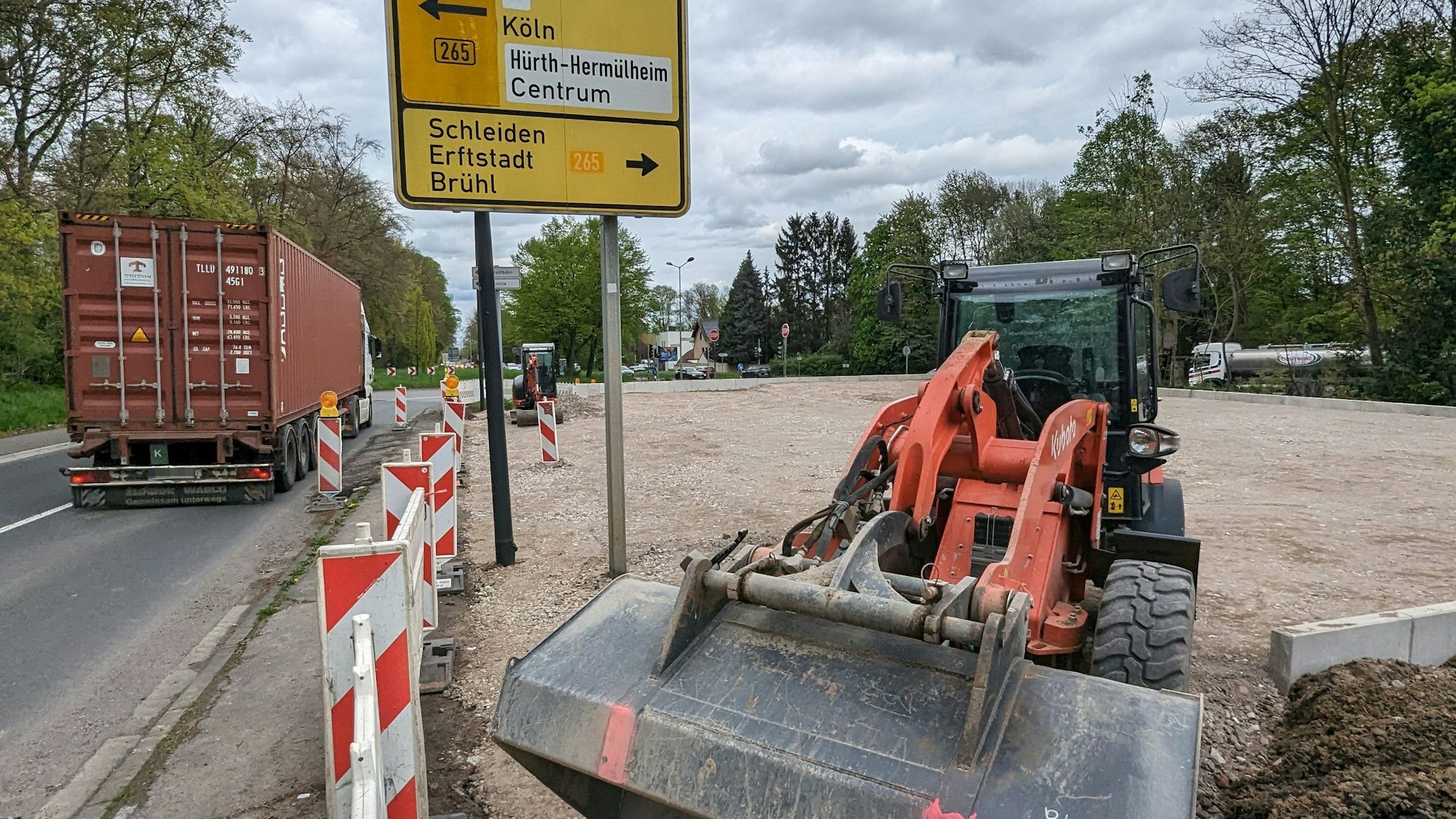Ein Bagger steht vor dem aufgeschütteten Fundament auf dem Grundstück an der Industriestraße. Im Bild auch eine große Wegweisertafel.