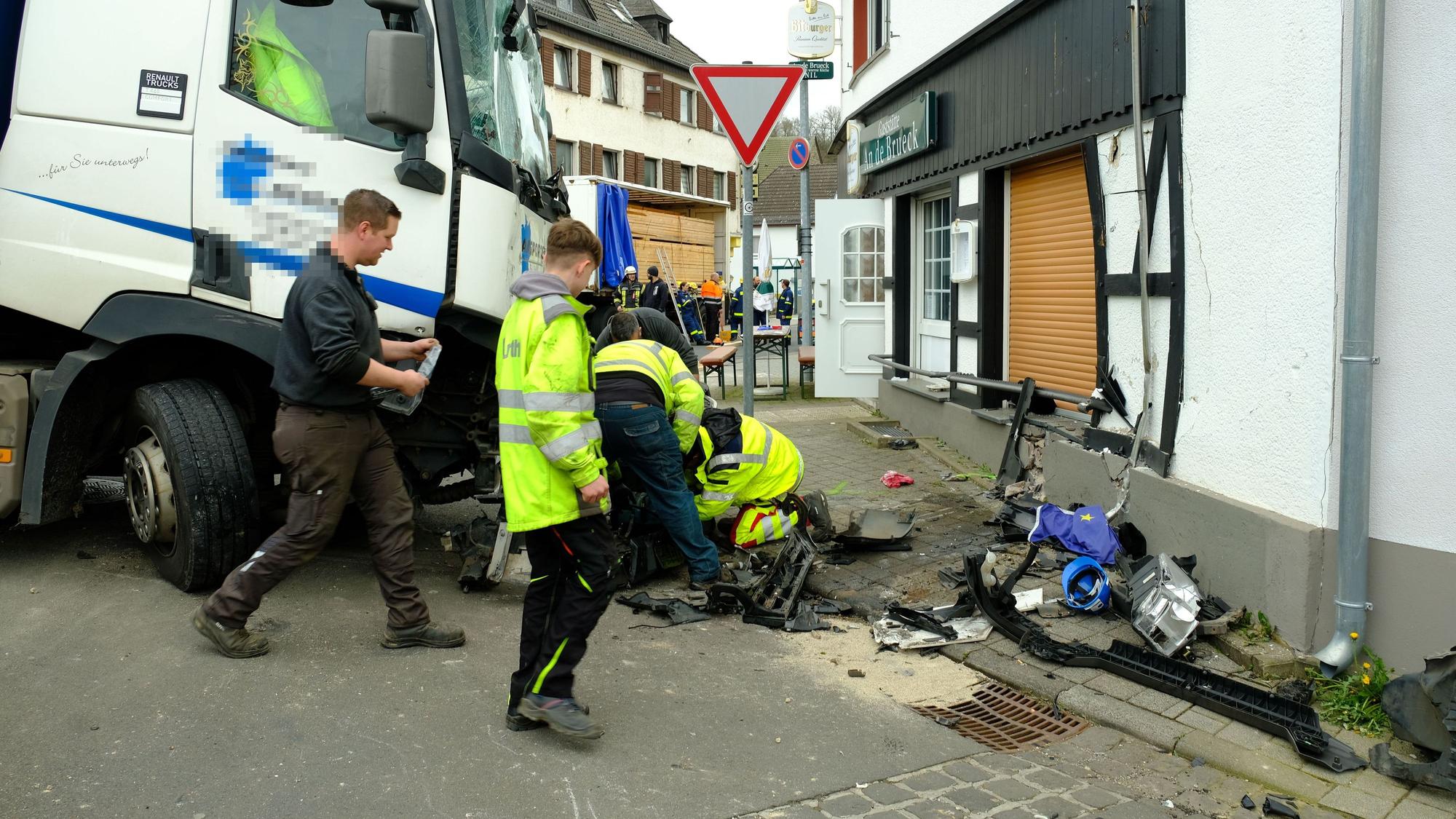 Mitarbeiter des Abschleppdienstes arbeiten am Lastwagen. Die Hauswand ist eingedrückt.