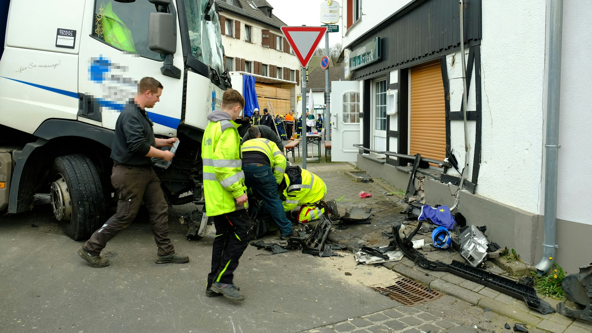 Mitarbeiter des Abschleppdienstes arbeiten am Lastwagen. Die Hauswand ist eingedrückt.