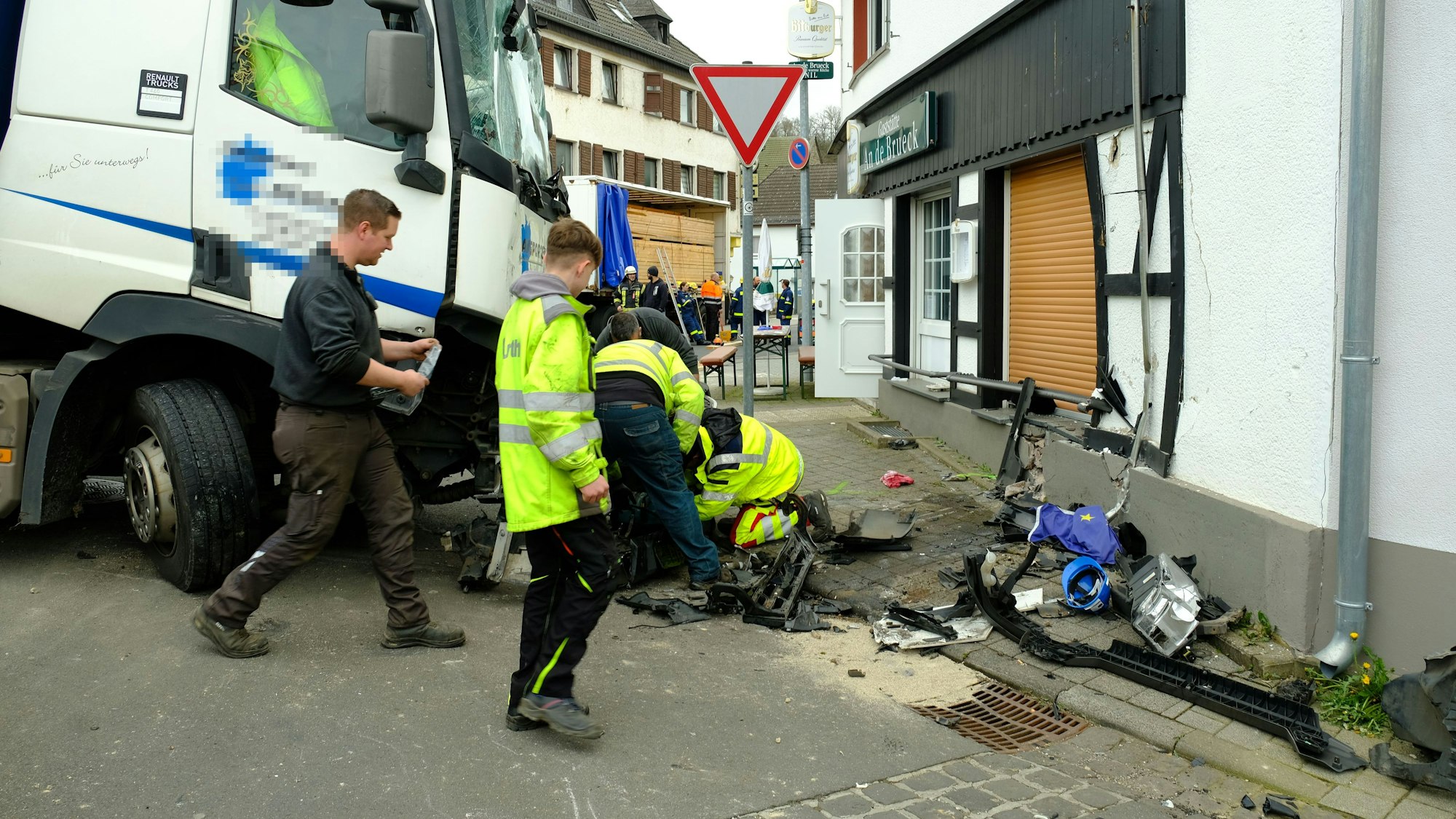 Mitarbeiter des Abschleppdienstes arbeiten am Lastwagen. Die Hauswand ist eingedrückt.