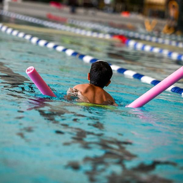 Ein Kind schwimmt mit Schwimmnudel durch ein Becken.