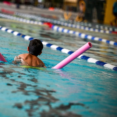 Ein Kind schwimmt mit Schwimmnudel durch ein Becken.