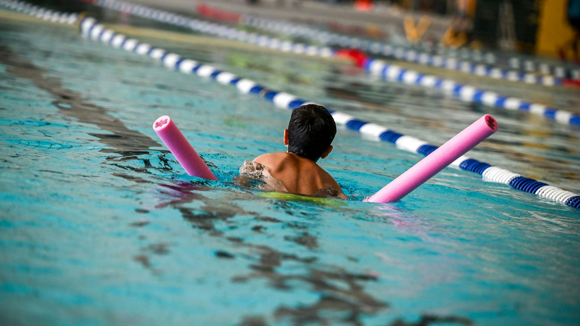 Ein Kind schwimmt mit Schwimmnudel durch ein Becken.