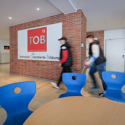 Zwei Schüler gehen am Logo der TOB Sekundarschule vorbei.
