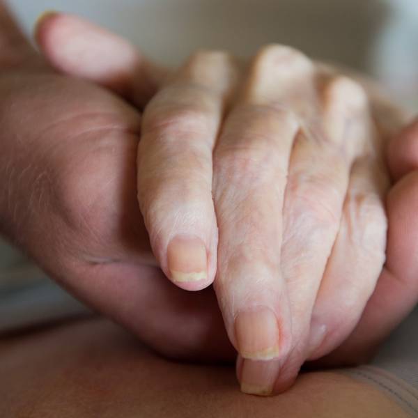 Ein Altenpfleger hält in einem Pflegeheim die Hand einer Frau.