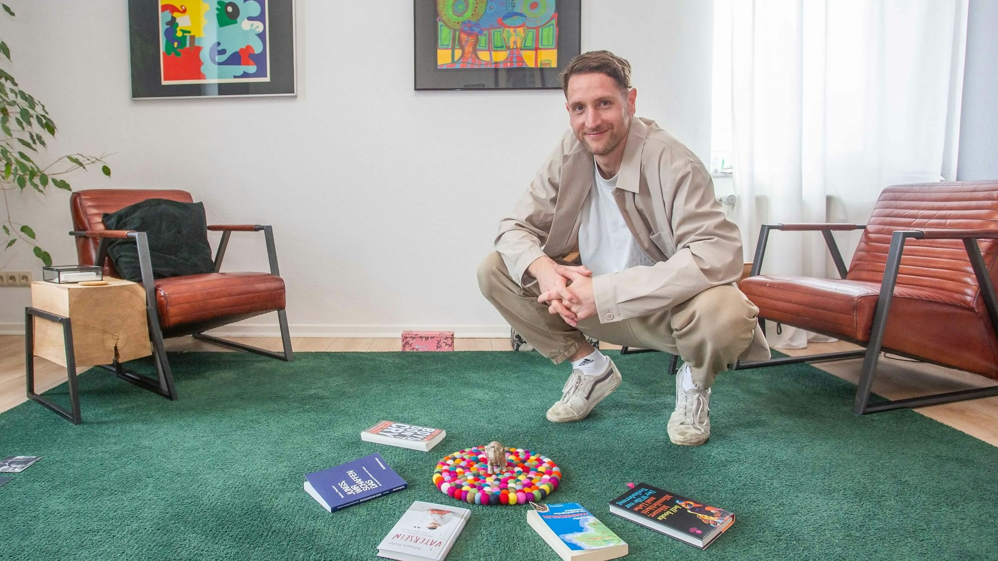 Matthias Stinn in der Hocke. Vor ihm auf dem Boden liegen mehrere Bücher, die in einem Halbkreis angeordnet sind.