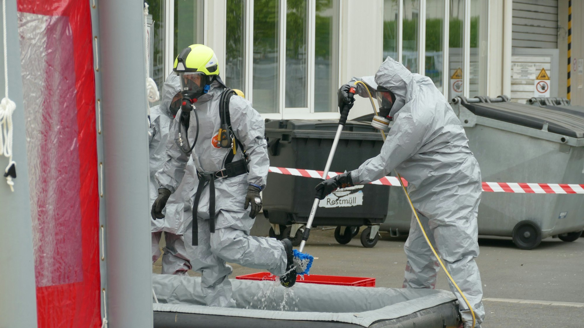 Feuerwehrleute reinigen am Dekontaminationsplatz gegenseitig ihre Schutzanzüge.