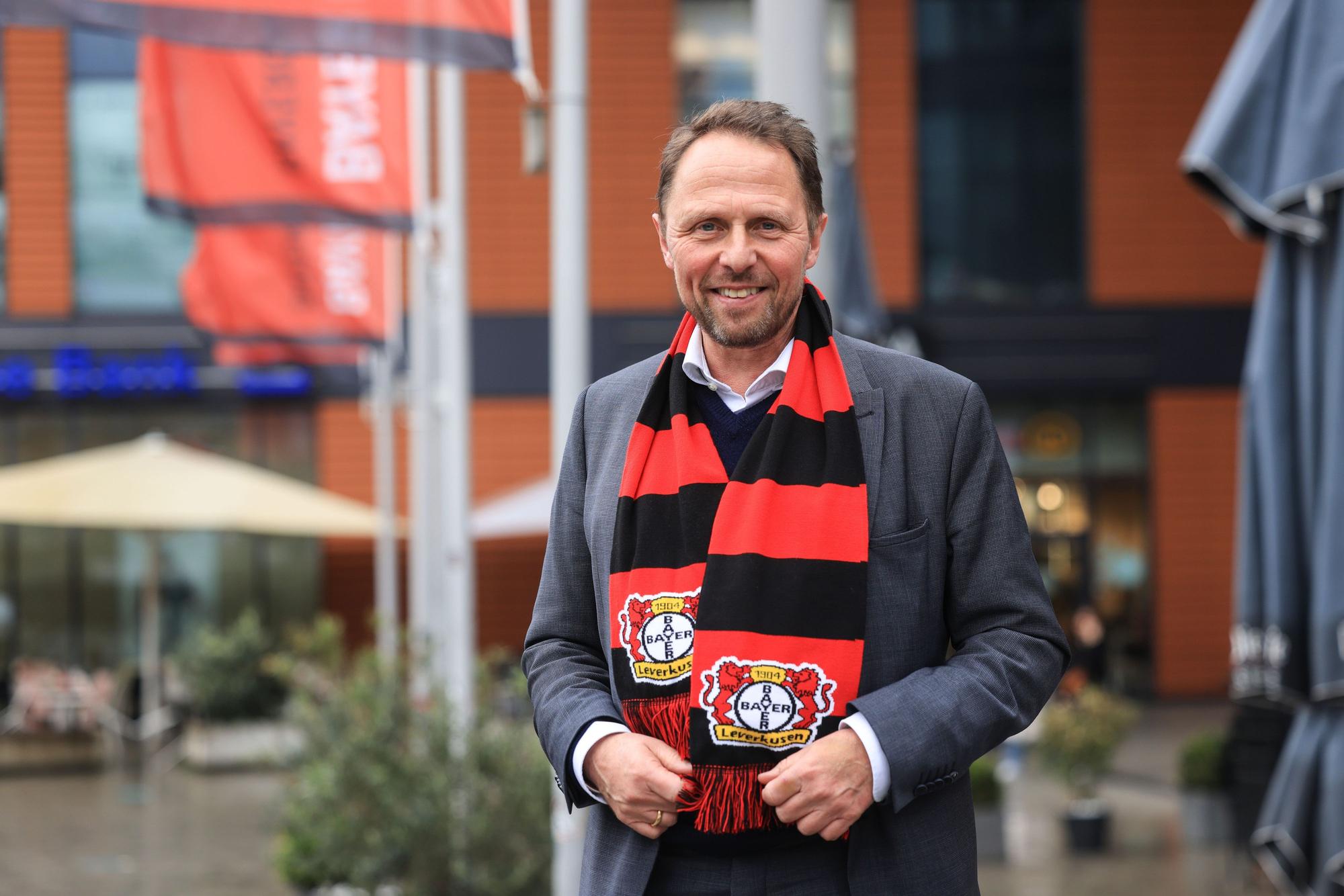 Uwe Richrath, Oberbürgermeister von Leverkusen, steht mit einem Fanschal vor dem Rathaus.