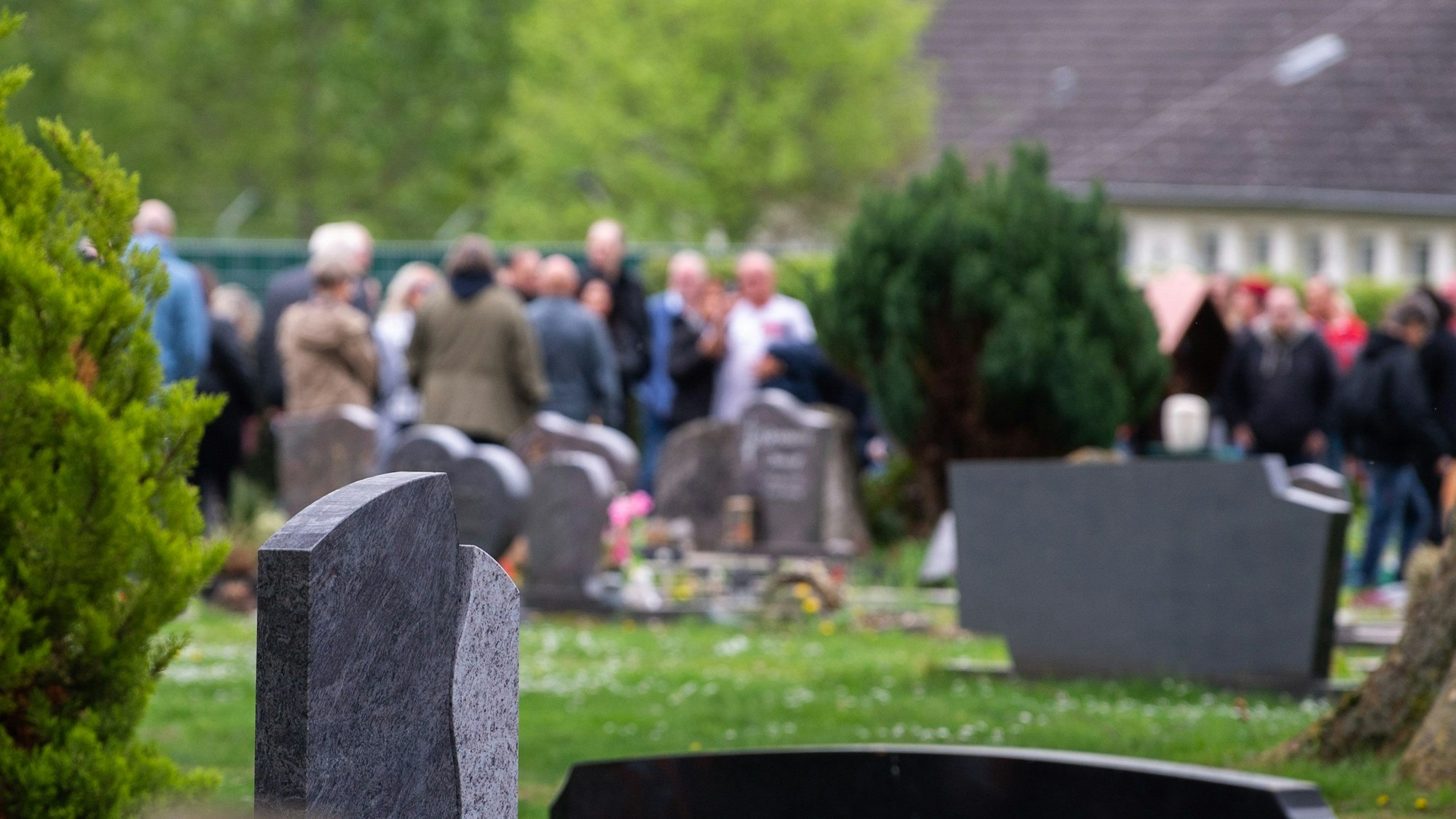 Trauergäste stehen auf einem Friedhof.