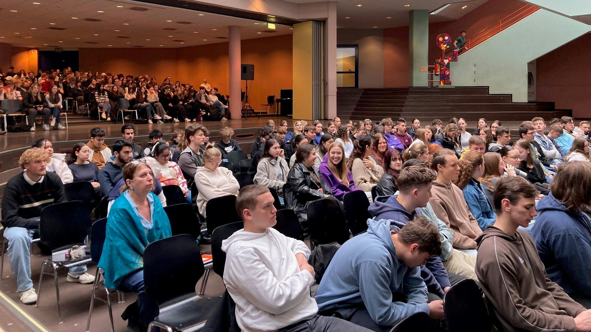 Jugendliche sitzen auf Stühlen in der Aula.