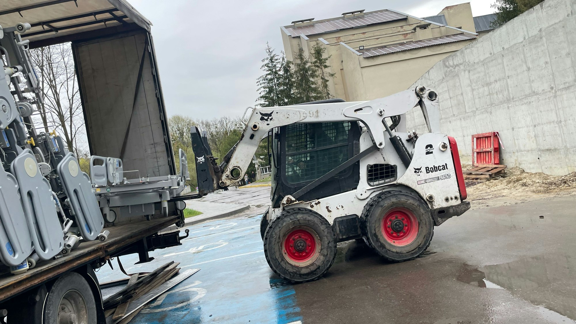 Ein Bobcat lädt ein elektrisches Krankenhausbett aus einem Sattelzug.