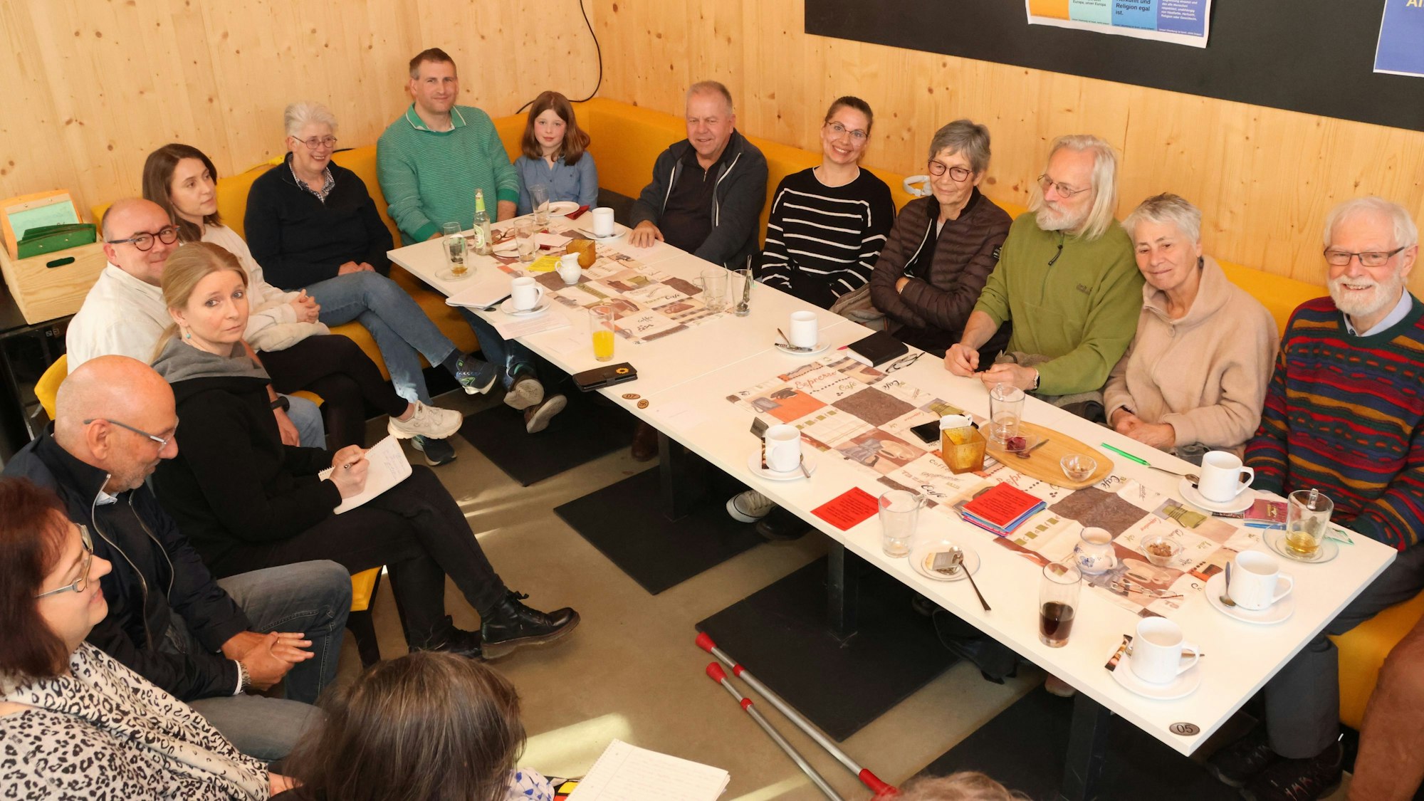 Mehrere Menschen sitzen gemeinsam um einen langen Tisch herum.