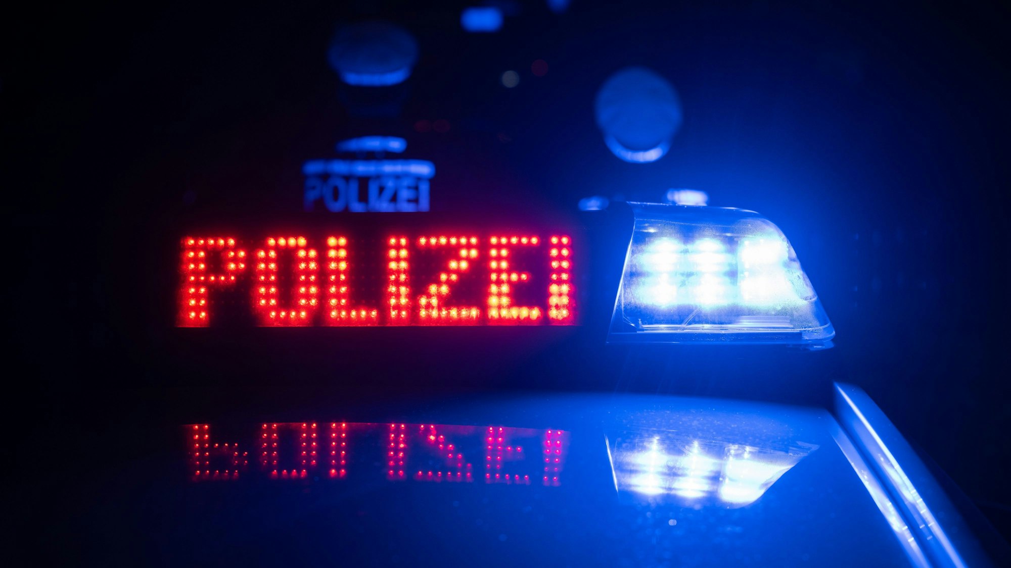 Zwei Einsatzkräfte stehen vor einem Polizeifahrzeug im Dunkeln. (Symbolbild)