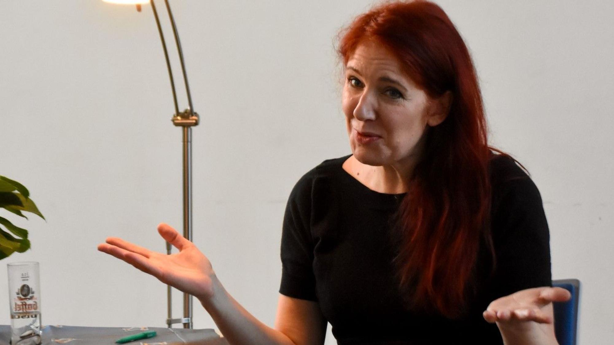 Eine Frau mit roten Haaren sitzt auf einem Stuhl neben einer Leselampe.