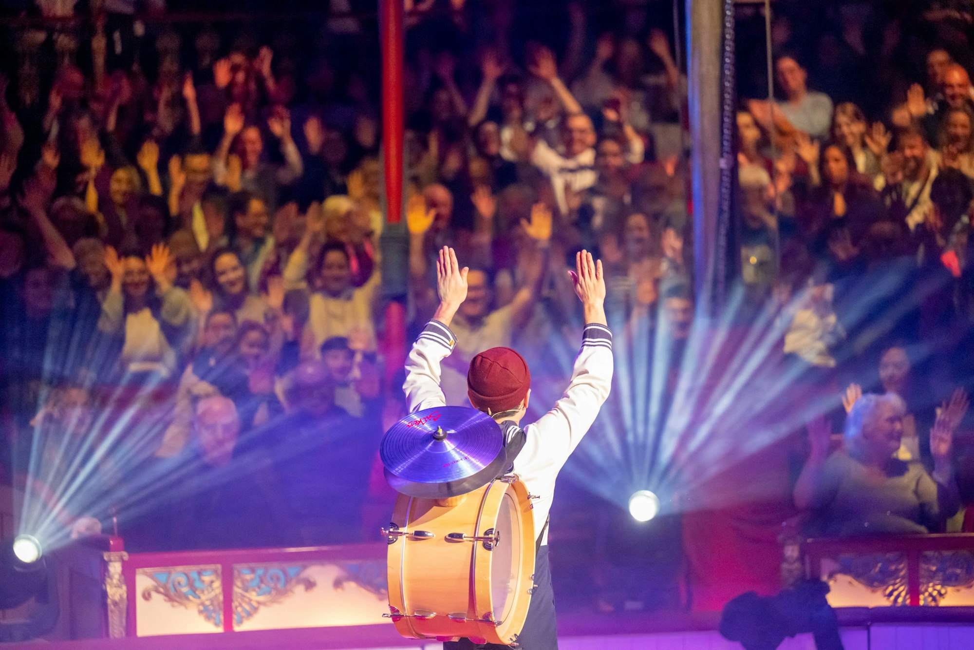 Ein Clown mit gehobenen Händen, das Publikum vor ihm macht es ihm nach.